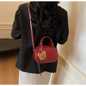 Détail du sac bowling en cuir verni rouge avec breloque ours et blazer noir élégant