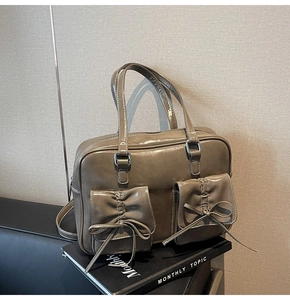 Macro view of dark brown patent leather tote featuring bow-decorated front flap pockets