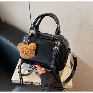 Détail d'un sac à main noir brillant en cuir PU avec fermeture éclair et charm d'ours en peluche