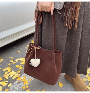 Brown suede tote bag with heart charm and bow detail in an autumn street scene