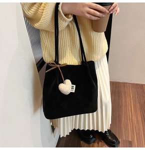 Detail of matte black suede tote bag featuring a white plush heart charm and bow