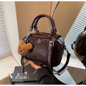 Détail du sac Boston marron foncé brillant avec un charmant porte-clés ours en peluche