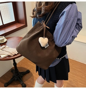 Detail of dark brown suede tote bag featuring a plush white heart charm and bow ribbon