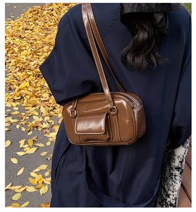 Close-up of brown patent leather handbag with white stitching in an autumn setting