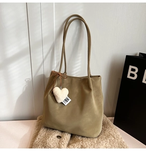 Detail of khaki suede tote bag with heart plush charm on a beige fleece jacket