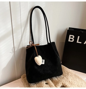 Close-up of black matte tote bag with heart charm and strap detail on soft beige fabric