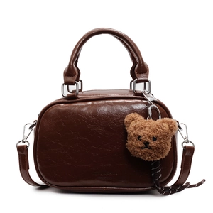 Retro brown PU leather baseball-shaped crossbody bag with a plush bear charm on white background