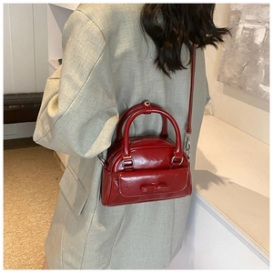Detail of red glossy Boston bag with bow accent worn over a grey blazer jacket