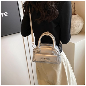 Close-up of a silver metallic Boston bag with bow detail and adjustable shoulder strap