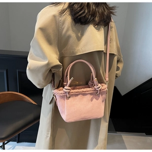 Model wearing a pink suede bucket bag with faux fur trim and gold-tone strap hardware