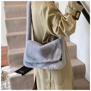 Zachte crossbodytas van imitatiebont in lichtgrijs blauw gedragen op een beige trenchcoat