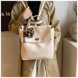 Detail eines cremeweißen Lederrucksacks mit Metalldrehverschluss und Leopardenherz-Anhänger
