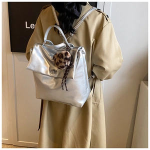 Silberner Metallic-Rucksack mit Leoparden-Bommel am Modell im khakifarbenen Mantel