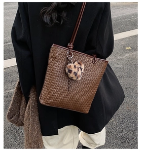 Detail of woven brown tote bag featuring a plush leopard heart charm and leather strap