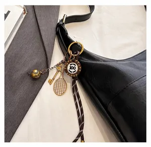 Détail d'un porte-clés raquette de tennis doré fixé sur un sac cabas en cuir noir