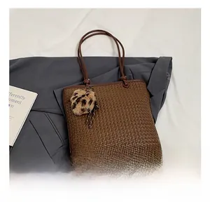 Close-up of brown woven tote bag featuring a leopard print plush charm detail
