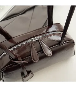 Detailed close-up of the smooth metal double zippers and shiny leather on the brown Boston bag