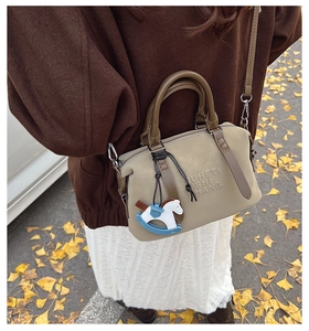Borsa Boston beige con manici marroni indossata a tracolla dalla modella in una strada autunnale