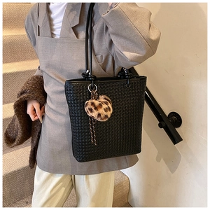 Detail of black woven tote bag with leopard heart charm worn by model in gray blazer