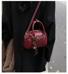 Detail of burgundy leather handbag with gold buckle and woven tassel on black coat