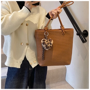 Detail of brown woven tote bag featuring fine texture and heart leopard plush charm
