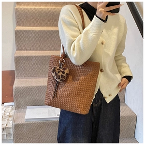 Close-up of brown woven tote bag with a leopard print heart pendant on a model