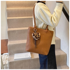 Close-up of brown woven tote bag with leopard print heart pendant on shoulder strap