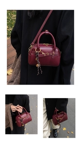 Macro shot of bordeaux leather boston bag with woven charm and golden hardware detail