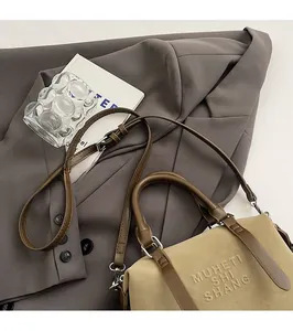 Dettaglio borsa Boston beige e marrone con logo a rilievo su abito grigio