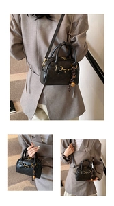 Detail of vintage black leather handbag with gold bell charm and shoulder strap