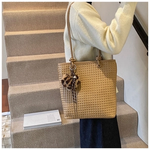 Detail of woven khaki tote bag with dual straps and a leopard print pom-pom charm
