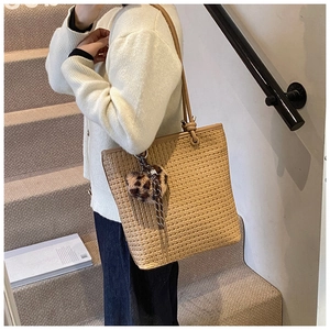 Straw tote bag detail with leopard print heart pendant and woven tassel accessory