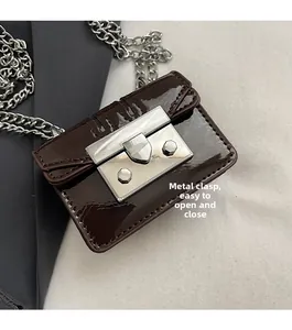 Detail of a dark brown patent leather mini bag with silver metal lock clasp and chain strap