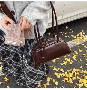 Outdoor shot of a dark brown glossy Boston shoulder bag with dual straps and autumn leaves