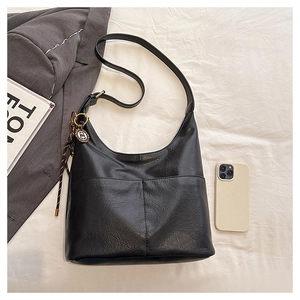 Détail du sac cabas demi-lune noir montrant le cuir grainé et le charme tissé décoratif