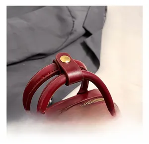 Detail of dark red leather handbag featuring gold metal buckles and a sturdy rounded handle