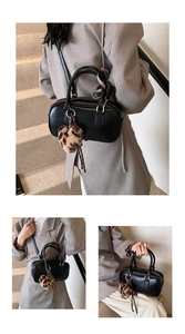 Close-up of black Boston bag with leopard print heart charm on stone stairs