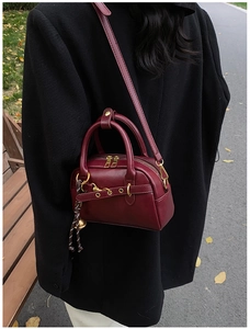 Detail of burgundy leather shoulder bag with gold hardware and woven rope pendant