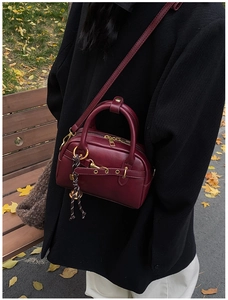 Close-up of deep red leather mini handbag with gold hardware on an autumn park bench