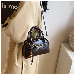 Detail of vintage brown Boston handbag with gold horsebit and bell charm on a beige coat
