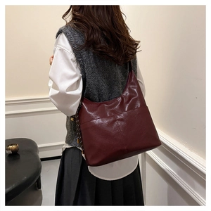 Detail of dark red faux leather tote bag with braided tassels and sleek half-moon hobo design