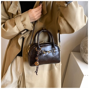 Close-up of vintage brown leather Boston bag with gold bell charm and zipper details