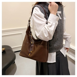 Close-up of brown tote bag with tennis racket charm and bicolor woven tassels
