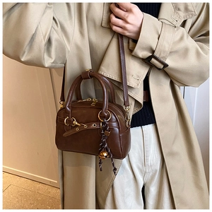 Detail of dark brown leather Boston bag with gold hardware worn with beige trench coat