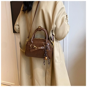 Brown vintage Boston bag featuring a metal lock and braided pendant on a beige coat