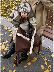 Detail of dark brown tote bag featuring a white faux shearling strap and gold hardware