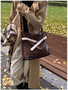 Detail of dark brown leather tote featuring white shearling trim and metal buckles