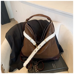 Detail of brown faux leather tote bag featuring a contrasting white fuzzy fleece shoulder strap