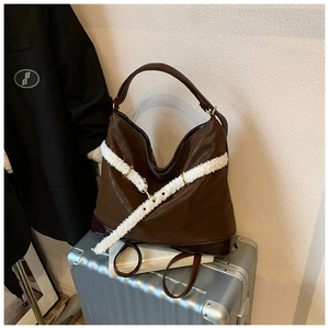 Detail of a brown tote bag with white faux fur trim and gold buckles on a metal suitcase
