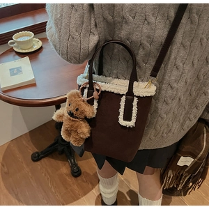 Dettaglio borsa a secchiello in camoscio marrone con bordo in shearling e ciondolo orsetto